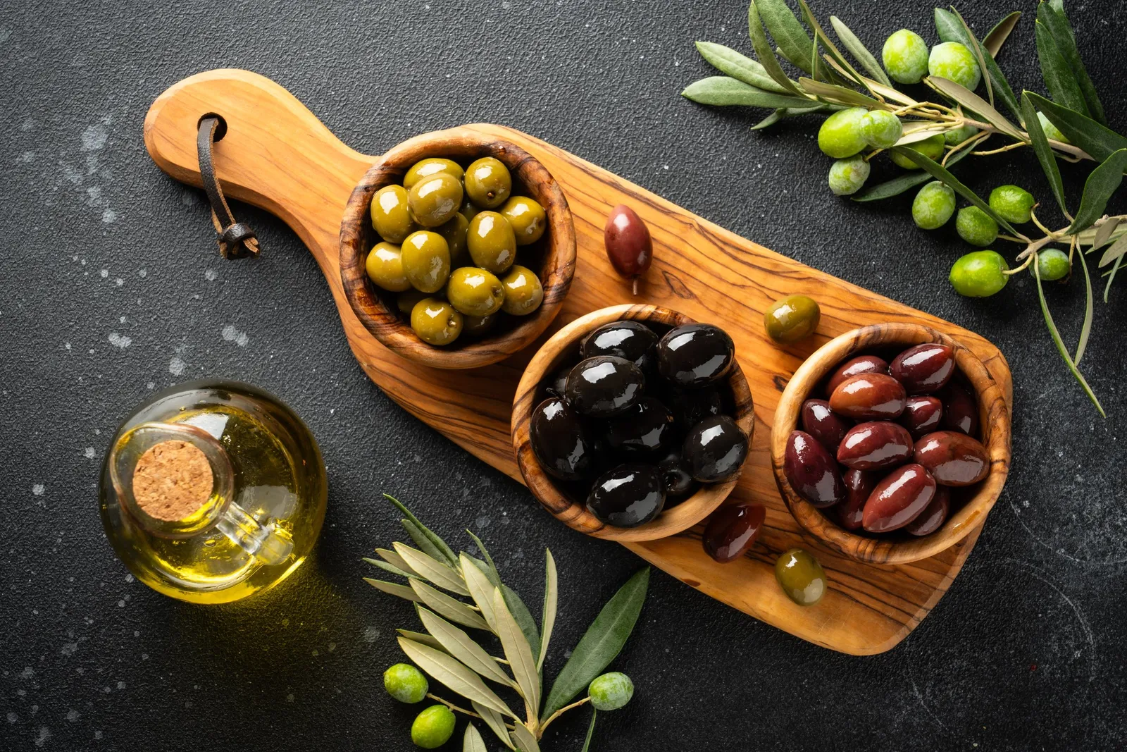 Olives and olive oil on a dark stone surface